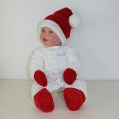 a baby wearing a red and white knitted santa hat sitting on the floor with his legs crossed