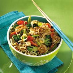 a bowl filled with noodles and vegetables on top of a blue napkin next to chopsticks