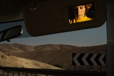 a woman is seen in the rear view mirror of a car as she drives through an arid area