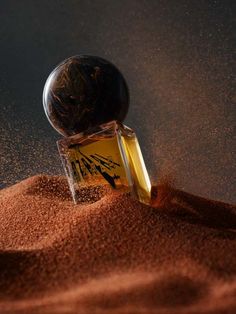 a bottle of perfume sitting on top of brown sand with a black ball in the middle