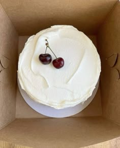 two cherries on top of a cake in a cardboard box with white frosting