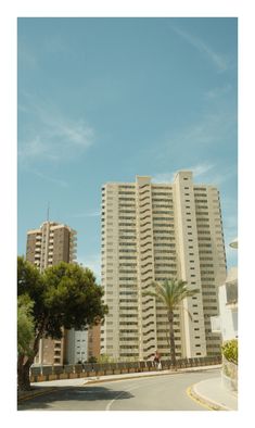 two tall buildings sitting next to each other on the side of a road in front of palm trees