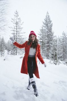 a woman in a red coat is playing in the snow with her hands out and smiling