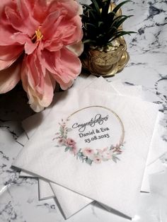 two napkins with flowers on them sitting next to a potted plant and a gold vase