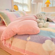 a teddy bear sitting on top of a bed covered in pink and blue blanketes