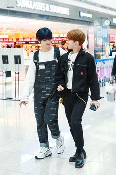 two young men walking through an airport with one holding onto the other's hand