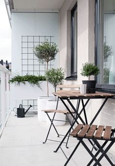 an outdoor table and chairs on a balcony with potted trees in the window sill