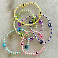 four bracelets with colorful beads and evil eyes are on the table next to each other