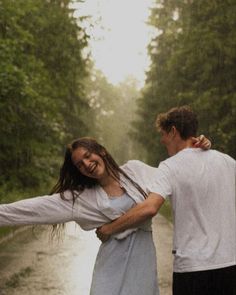 a man and woman walking down a rain soaked road in the rain with their arms around each other