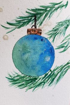 a blue ornament hanging from a pine tree with watercolors on it