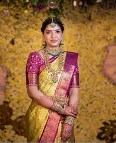 a woman in a yellow and pink sari standing next to a floral wallpaper