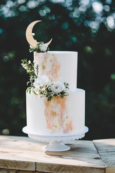 a three tiered cake with flowers and a crescent on the top is sitting on a wooden table