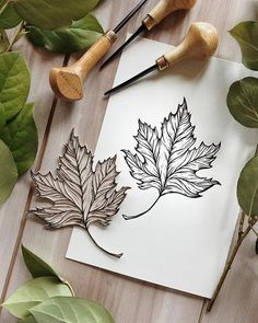 some leaves are sitting on top of a piece of paper next to paintbrushes