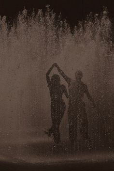 two people standing in front of a fountain with water shooting up from the top and behind them