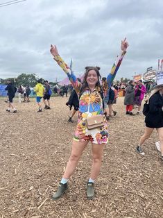 a woman with her arms in the air at an outdoor music festival, surrounded by other people