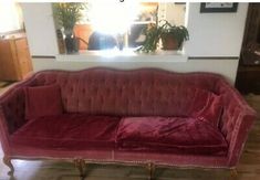 a red velvet couch sitting on top of a hard wood floor next to a window