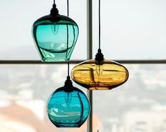 three different colored glass lights hanging from a ceiling in front of a window with cityscape