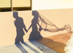 the shadow of two people holding hands with a veil over their heads on a wall