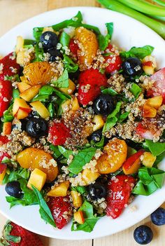 a white plate topped with fruit salad next to blueberries and asparagus on top of a wooden table