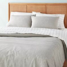 a bed with white and grey linens in a blue room, next to a wooden headboard