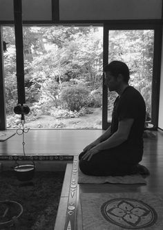 a man sitting on top of a yoga mat in front of a large glass window