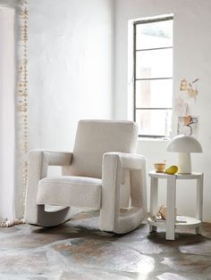 a white rocking chair sitting next to a table with a lamp on top of it