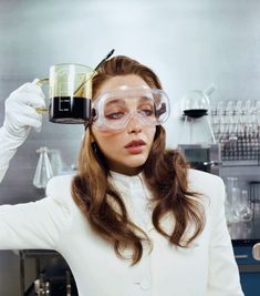 a woman wearing goggles and holding a beaker over her head