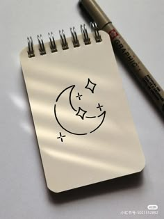 a notepad with a drawing of a crescent moon and stars on it next to a marker pen