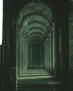 an empty hallway with arches and columns leading to the light at the end is seen in black and white