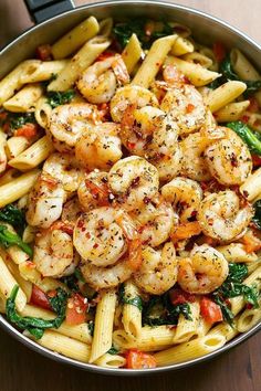 pasta with shrimp, spinach and tomatoes in a skillet on a wooden table