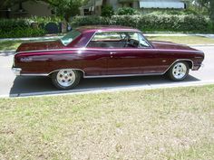 a maroon car is parked on the side of the road in front of a house