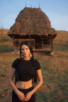 a woman with long hair standing in front of a small hut on the grass field