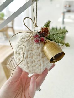 a hand holding a christmas ornament with a bell