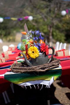 the table is set up with red and white tables cloths, colorful flowers in a coffee cup