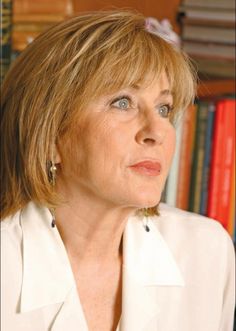 a woman with blonde hair and blue eyes looking off to the side in front of bookshelves