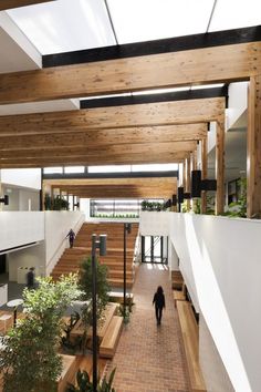 a person walking down a brick walkway in a building with wooden ceilings and stairs leading up to the second floor