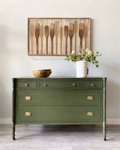 a green dresser with wooden spoons hanging on the wall above it and a white vase filled with flowers