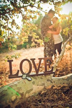 a man and woman standing next to each other near a tree trunk with the word love written on it