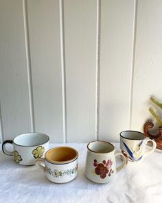 three coffee mugs sitting next to each other on top of a white tablecloth