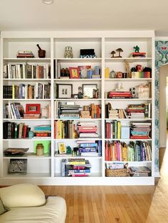 a white bookcase filled with lots of books on top of a hard wood floor