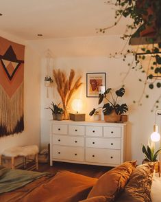 a bed room with a neatly made bed and some plants on the dresser next to it