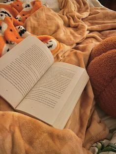 an open book sitting on top of a bed next to two stuffed animals and blankets