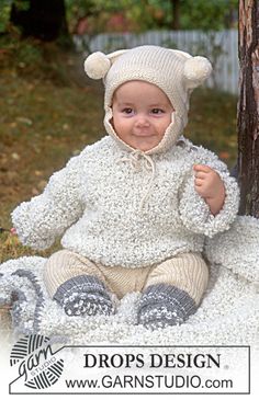 a baby wearing a knitted bear outfit sitting in the grass next to a tree