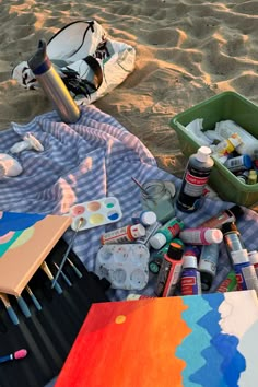 an artist's palette, watercolors and other art supplies on a blanket at the beach