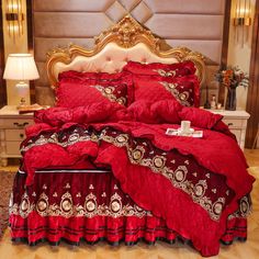 a bed with red comforter and pillows on it in front of a gold headboard