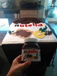 a hand holding a bottle of nutella in front of a cake on a table