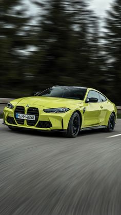 a bright yellow sports car driving down the road with trees in the backround