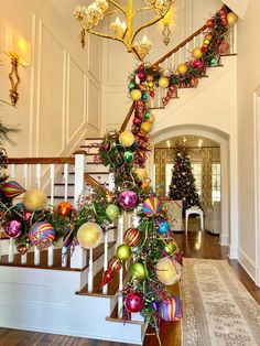 a staircase decorated for christmas with ornaments on the bannister and tree in the background