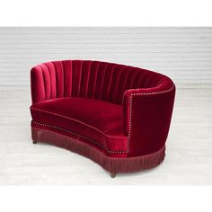 a red velvet sofa with fringe trim and studded details on the arm, sitting in front of a white brick wall