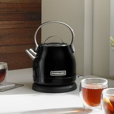 a black tea kettle sitting on top of a table next to a cup of tea